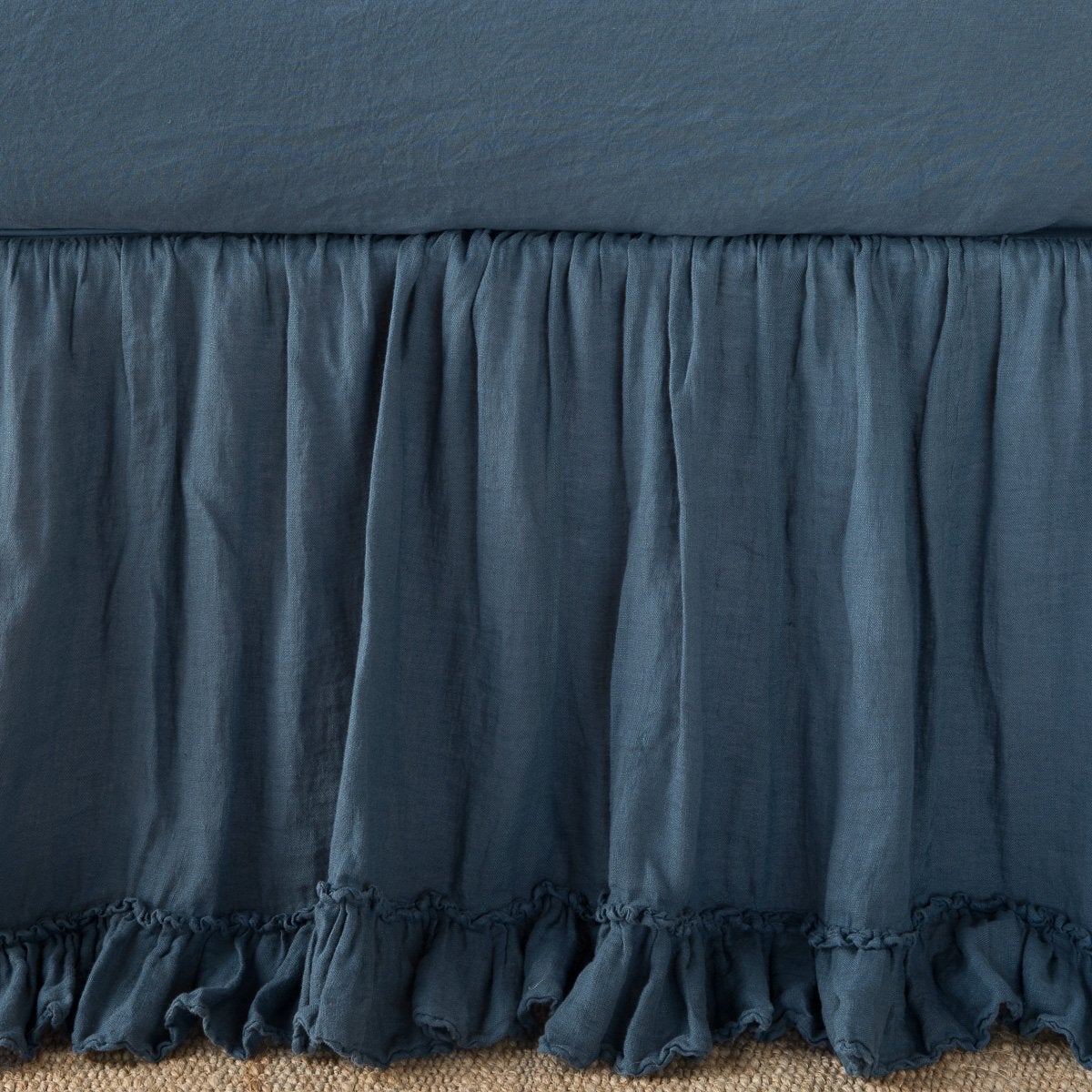 Midnight linen bed skirt with gathered ruffle hem, draped on a bed frame.