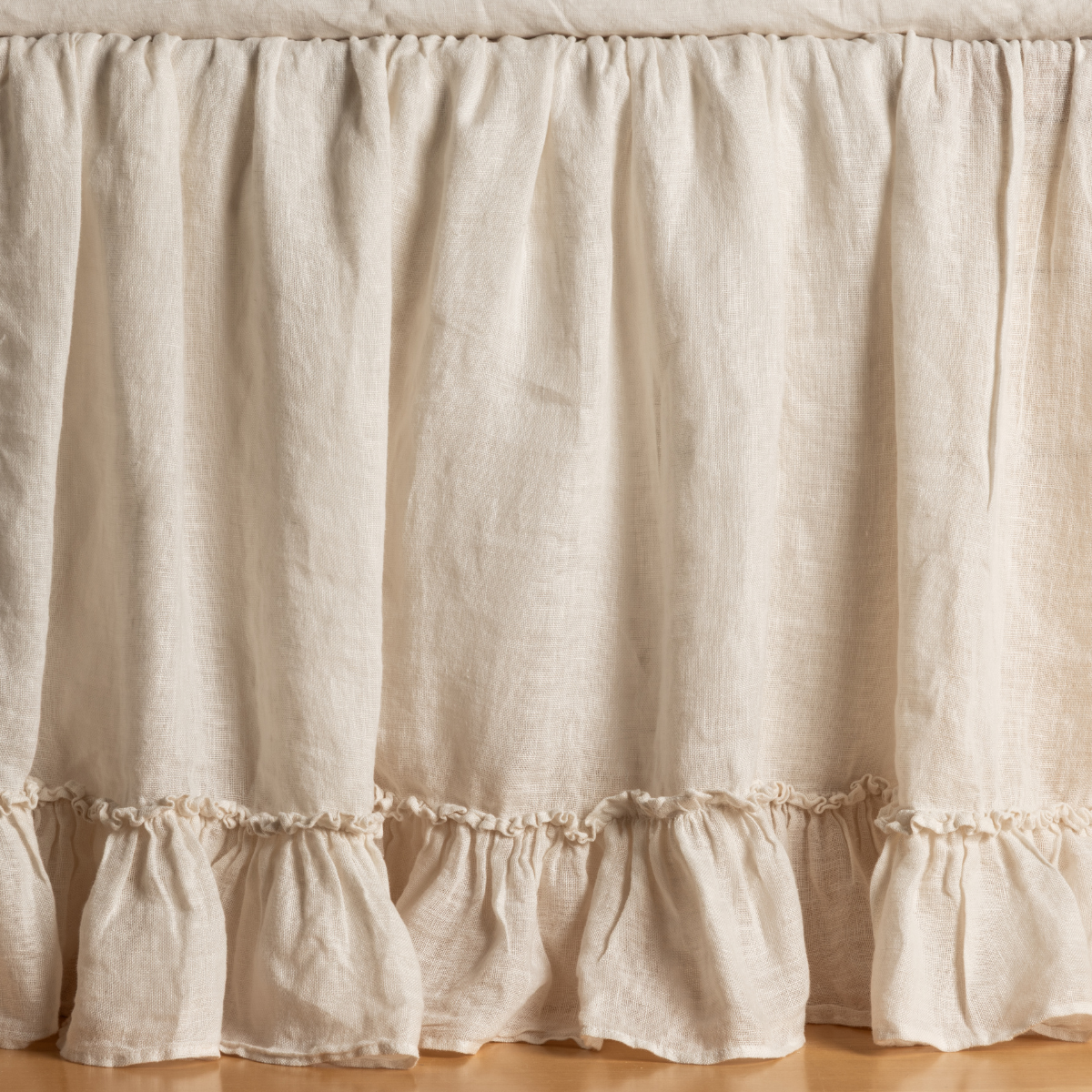 Natural linen bed skirt with double ruffle hem detail, gathered panels draping to floor.