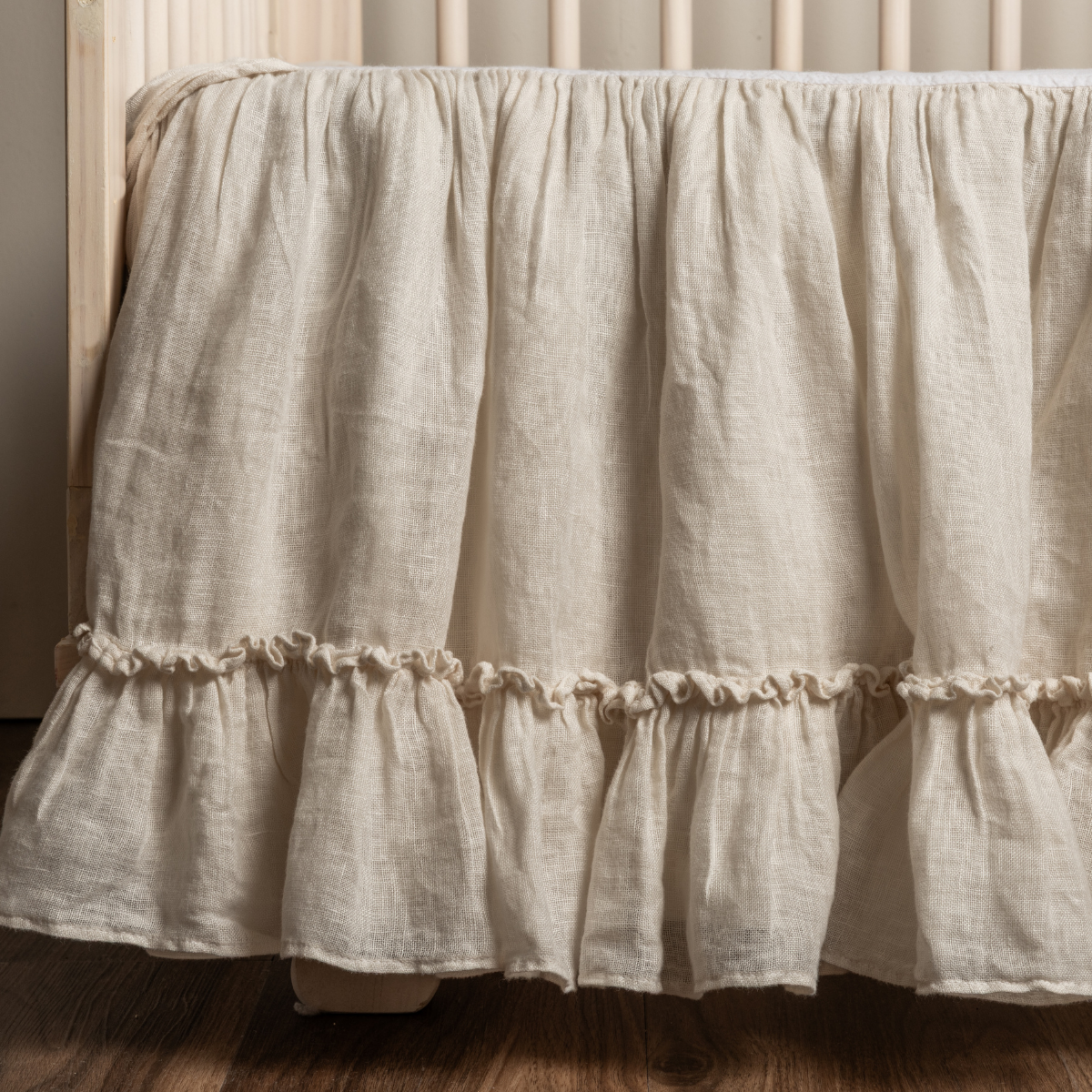 Natural linen crib skirt with double ruffle hem detail, draped on a crib frame.