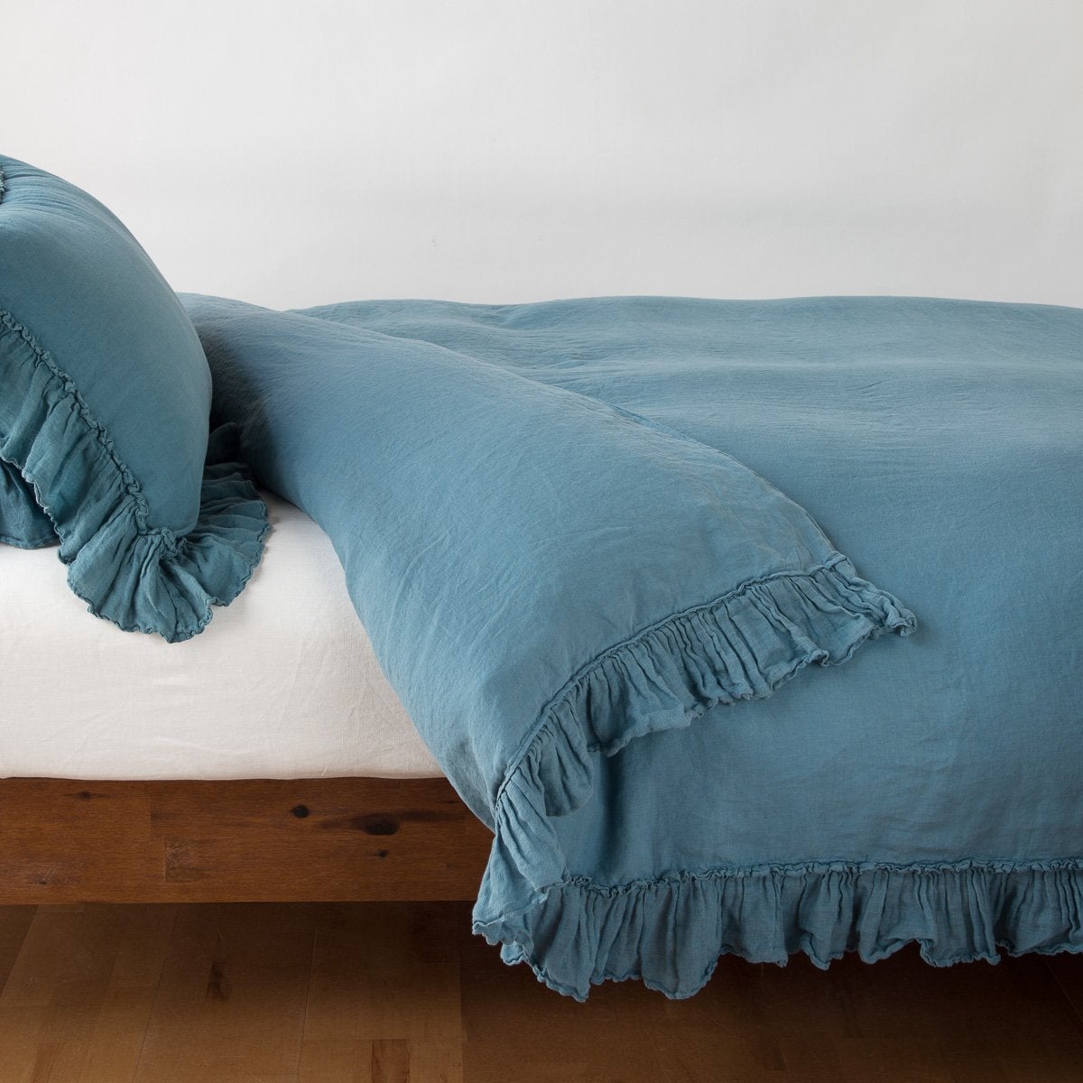 Cenote linen duvet cover with ruffled trim, styled on a bed with matching pillows.