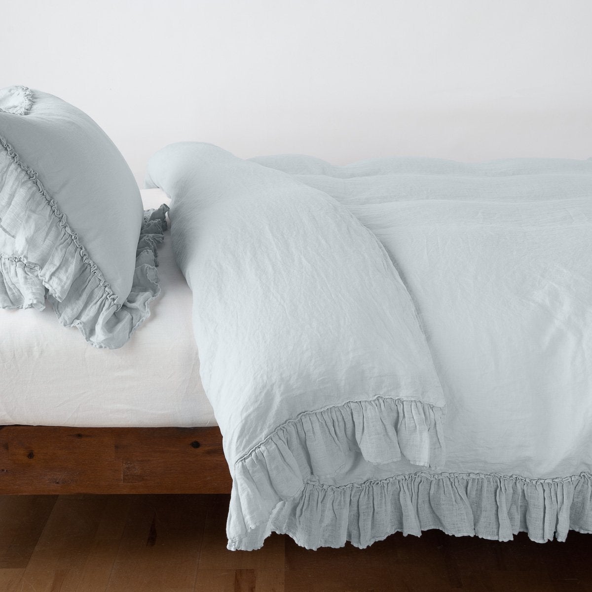 Ruffled hem detail on Bella Notte Linen Whisper duvet cover in Cloud on a wood bed frame.