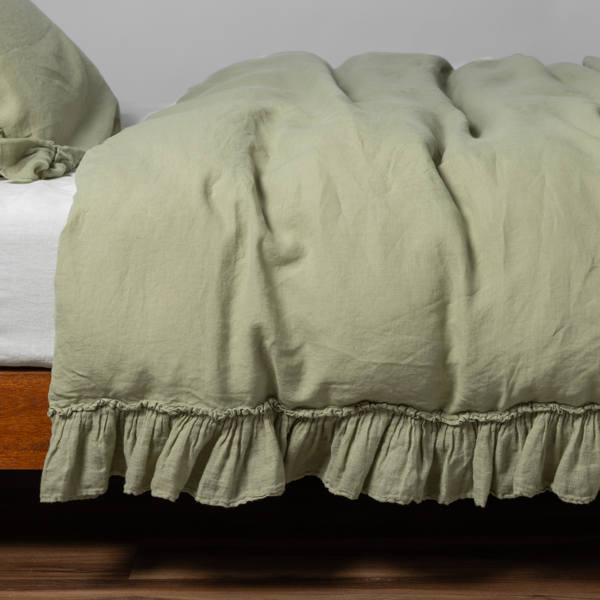 Ruffled hem detail of Bella Notte Linen Whisper duvet cover in Desert Sagge on a wood bed.