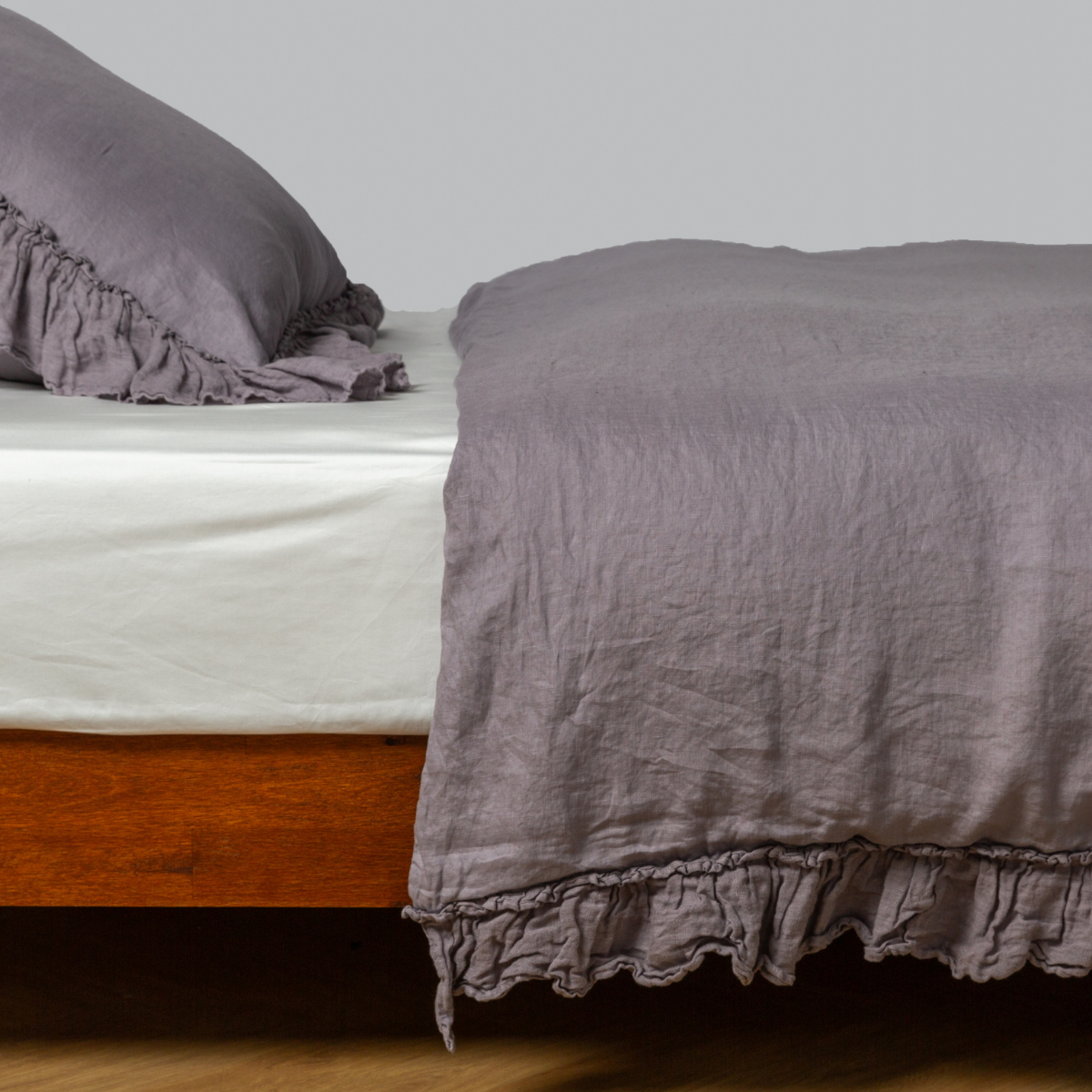 Ruffled hem detail of Bella Notte Linen Whisper duvet cover in French Lavender on a wood-frame bed.