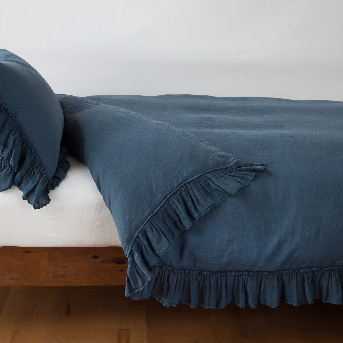 Midnight linen duvet cover with delicate ruffle trim, styled on a bed with matching pillow.