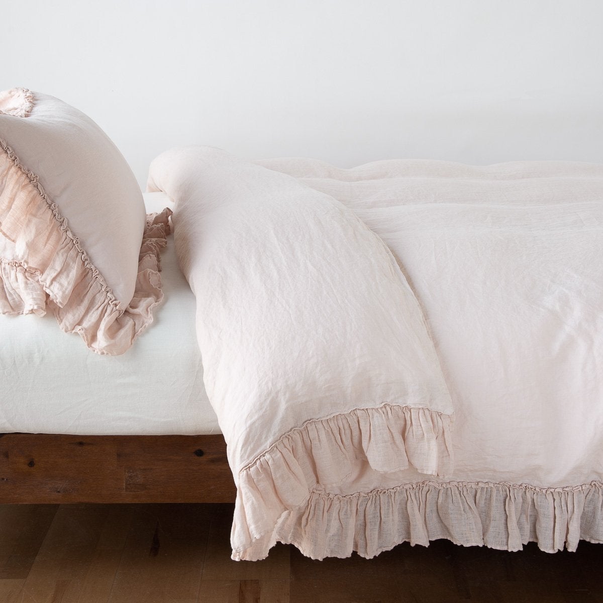 Ruffled hem detail on Bella Notte Linen Whisper duvet cover in Pearl, styled on low wood bed.