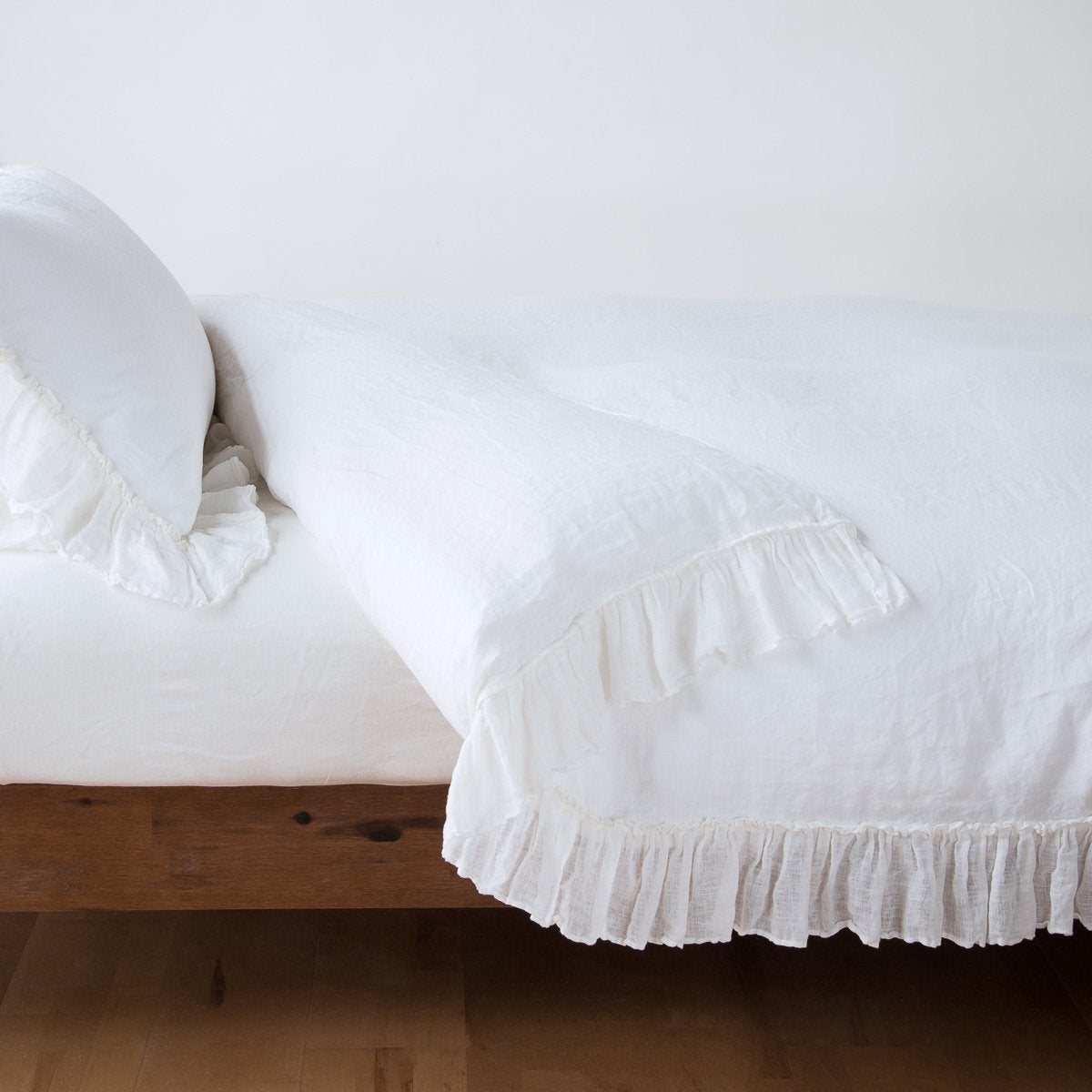 Bella Notte Linen Whisper duvet cover in White with ruffled hem, styled on a wood bed.