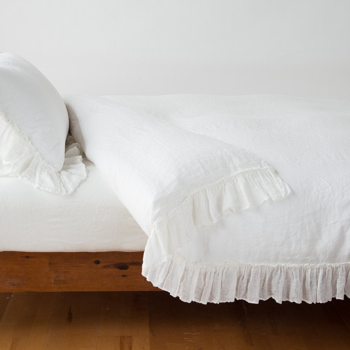 Bella Notte Linen Whisper duvet cover in Winter White with ruffled trim on a wood-frame bed.