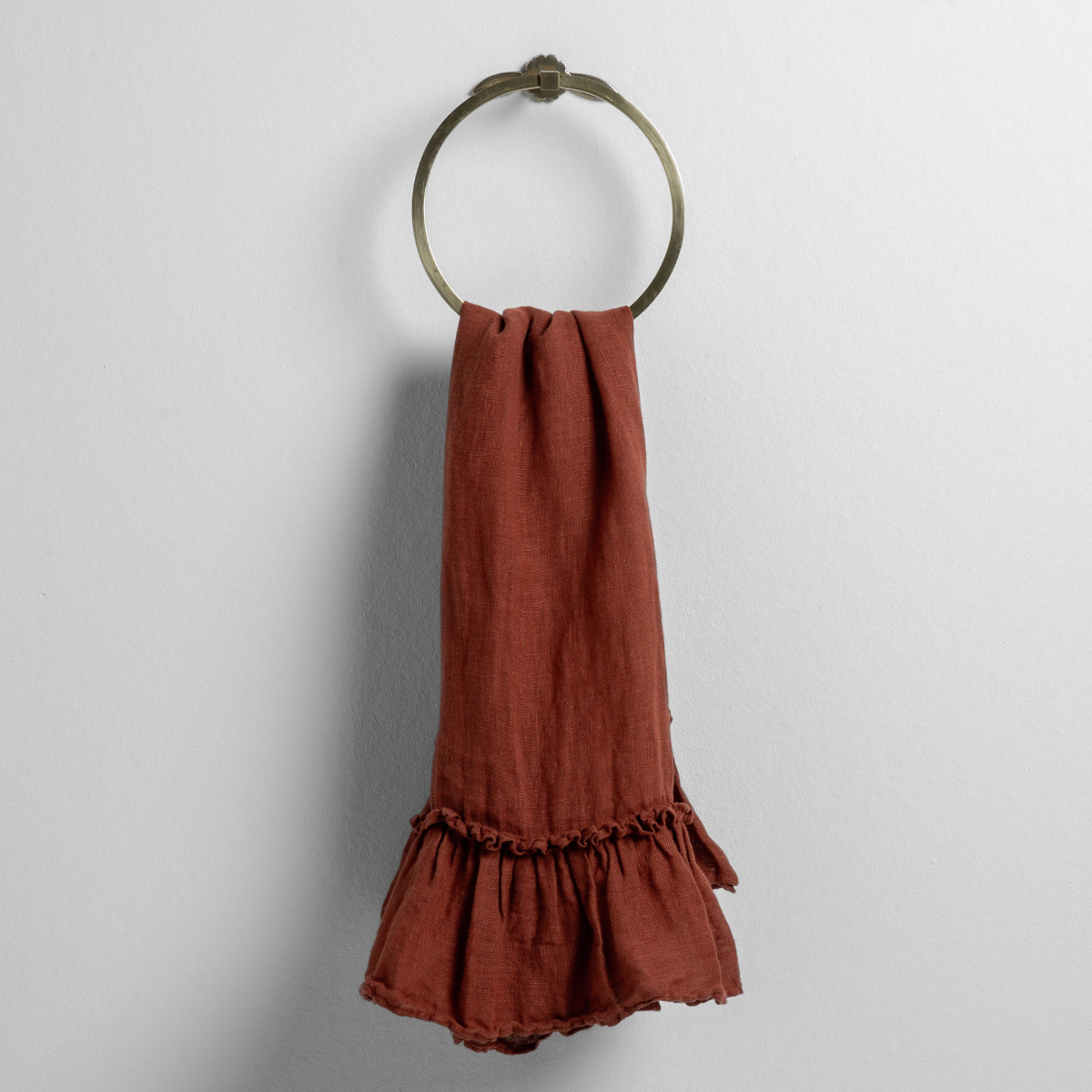 Autumn linen guest towel with ruffled hem, draped through a brass ring on a white wall.