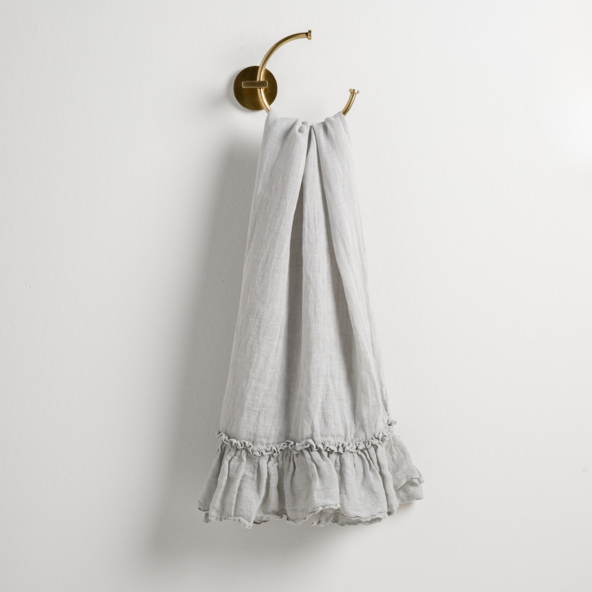 Bella Notte Linen Whisper guest towel in Cloud draped on brass wall hook, ruffled hem detail.