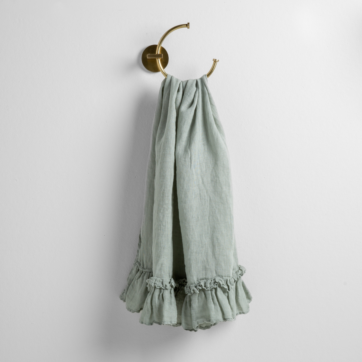 Eucalyptus linen guest towel with ruffled hem, hanging from a brass ring hook.