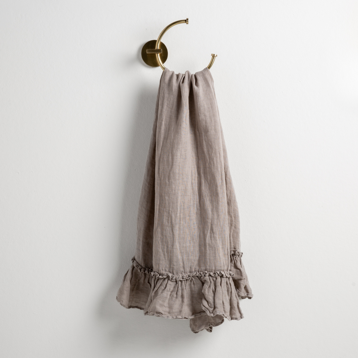 Fog linen guest towel with ruffled hem, draped over a brass ring hook.
