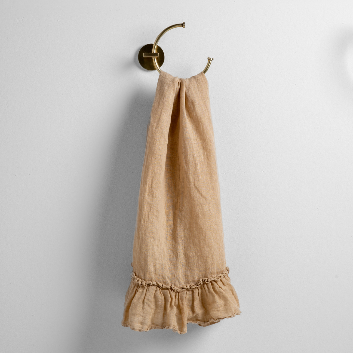 Honeycomb linen guest towel with ruffled hem, hung on a brass ring hook.