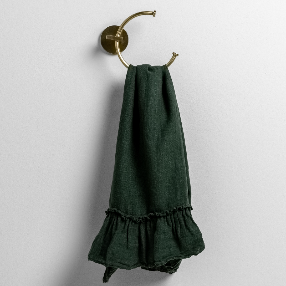 Juniper linen guest towel with ruffle hem, draped over a brass ring towel holder.