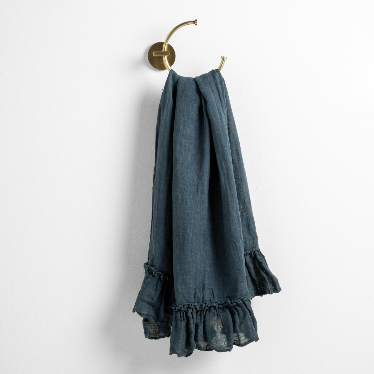 Midnight linen guest towel draped over brass ring hook, showing ruffled hem detail.