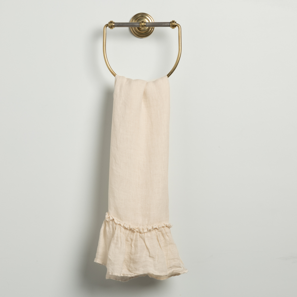 Natural linen guest towel with ruffle hem, hung on a brass ring towel holder.