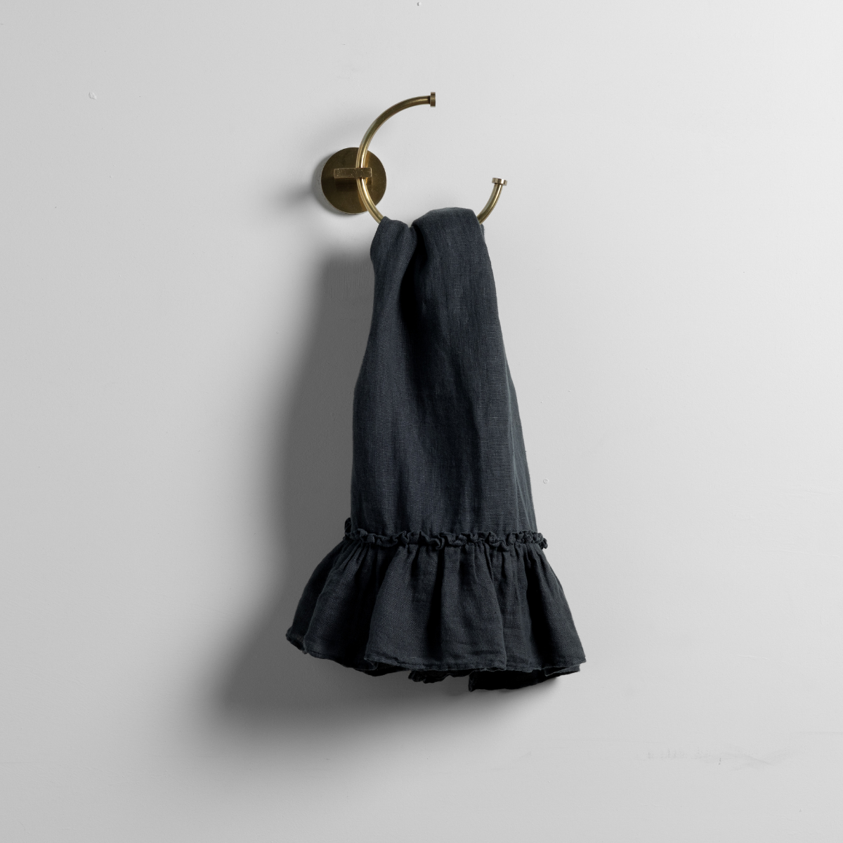 Slate linen guest towel with ruffled hem, hung on a brass double hook.