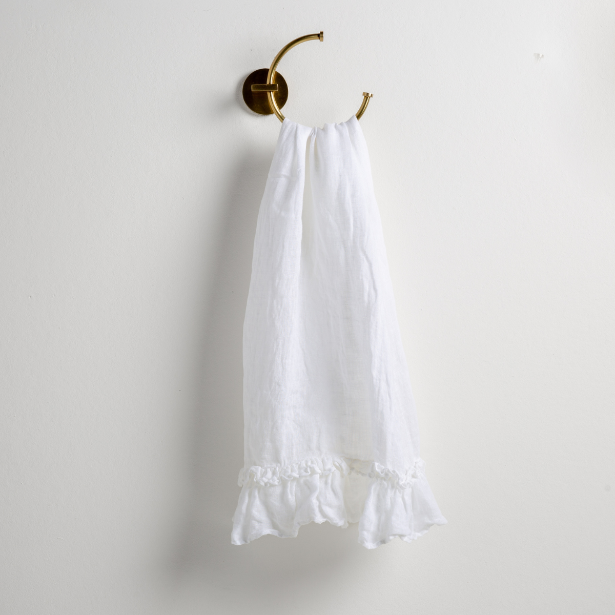 Bella Notte Linen Whisper guest towel in White with ruffled hem, hung on brass wall hook.