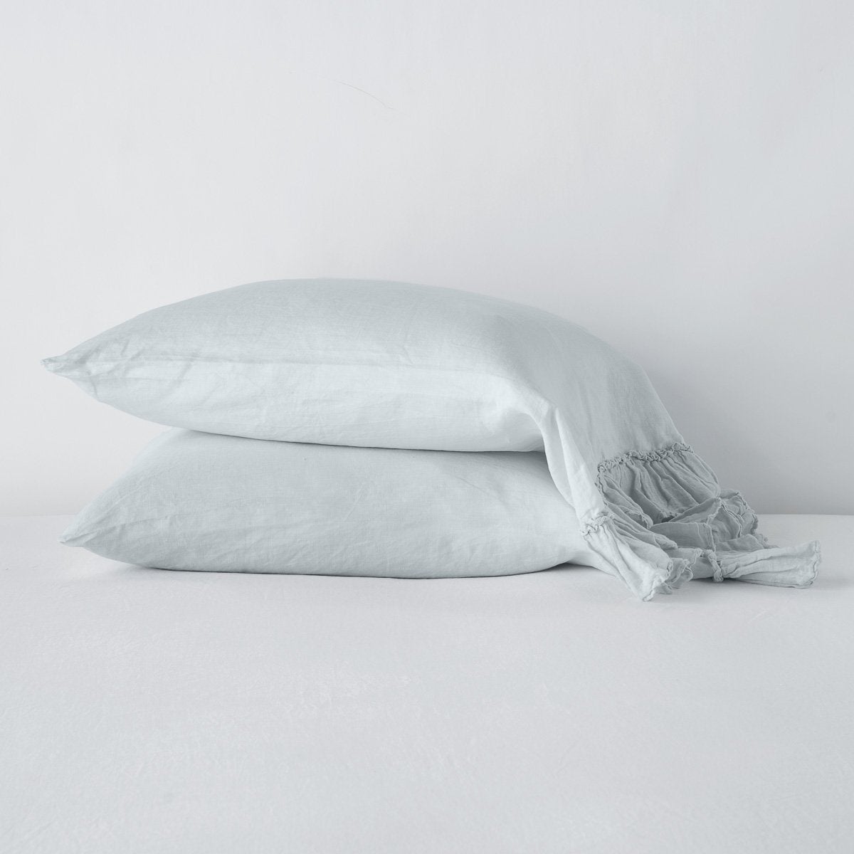 Two stacked Cloud linen pillowcases with relaxed ruffle trim, softly draped on white surface.