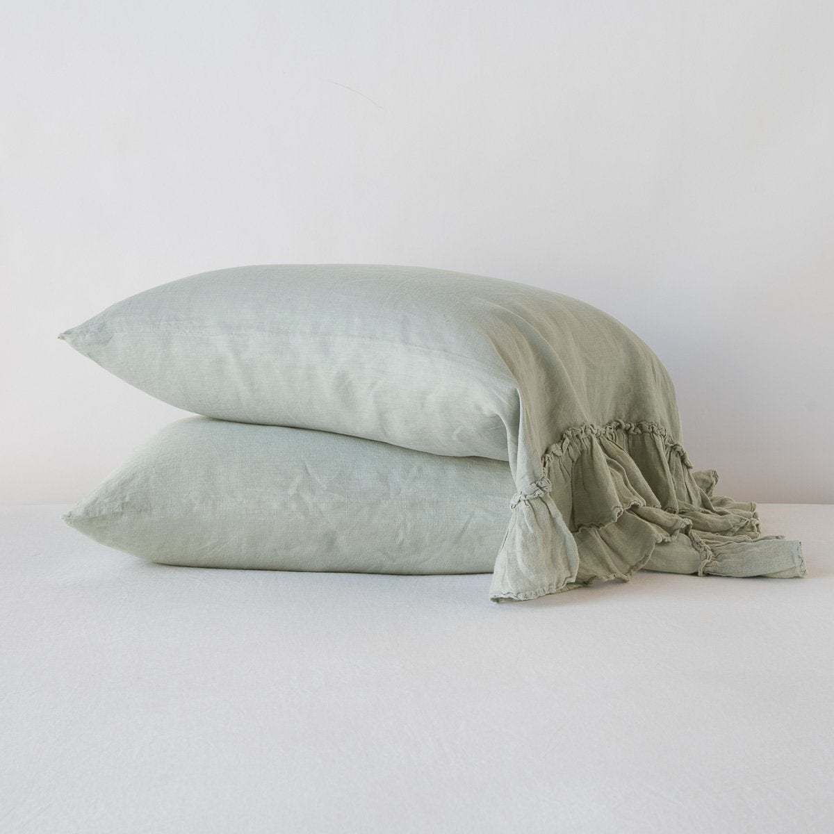 Two Bella Notte Linen Whisper pillowcases stacked, Eucalyptus, with ruffled edge detail visible.