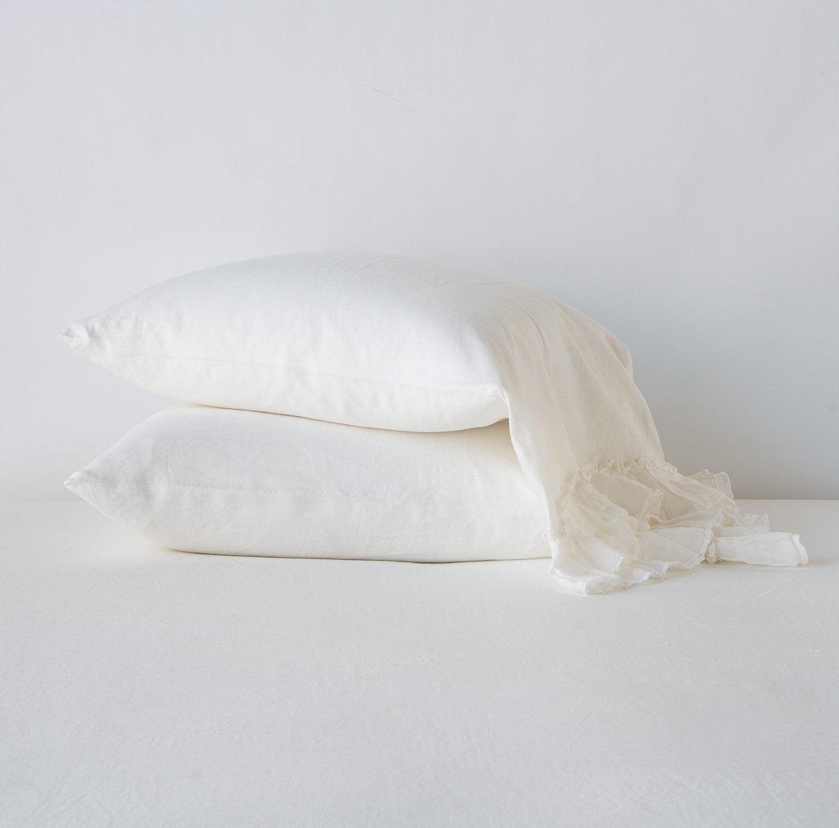 Two stacked Winter White linen pillowcases with delicate frayed ruffle trim detail.