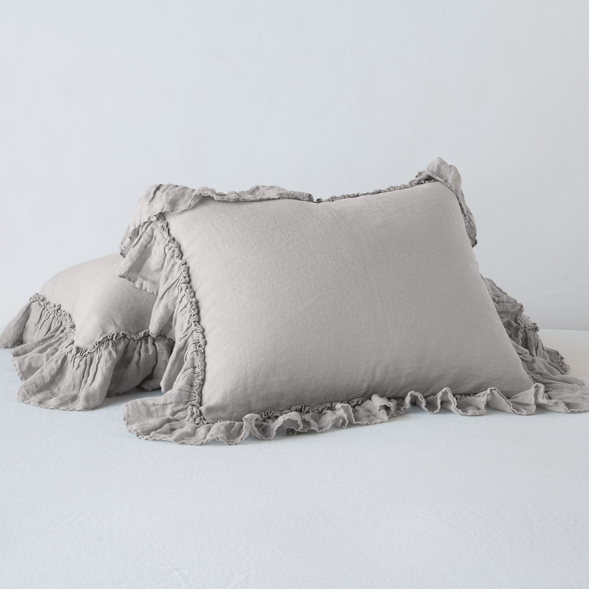 Two Bella Notte Linen Whisper shams in Fog with delicate ruffled trim, styled on a white surface.