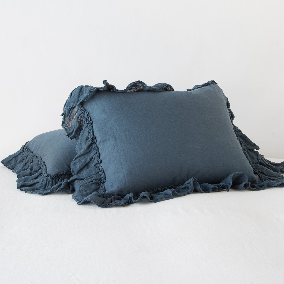 Ruffled edges of Bella Notte Linen Whisper shams in Midnight, stacked against a white backdrop.