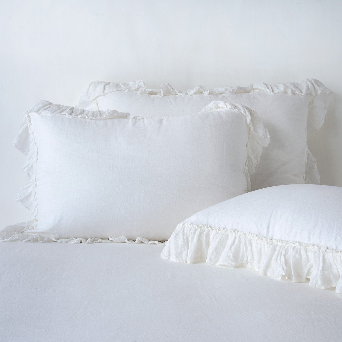 Bella Notte Linen Whisper sham in White with delicate ruffle trim, styled on a bed.