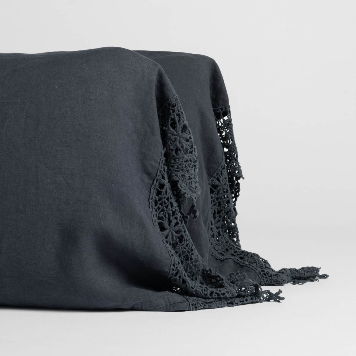 Slate linen pillowcase with intricate floral crochet lace trim and fringe detail.