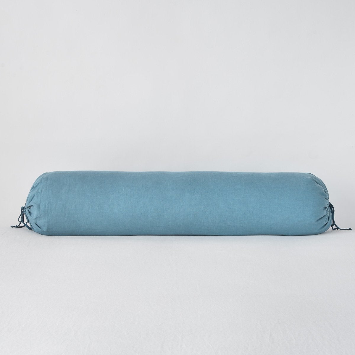Bella Notte Linen bolster in Cenote, with gathered tie ends on a white surface.
