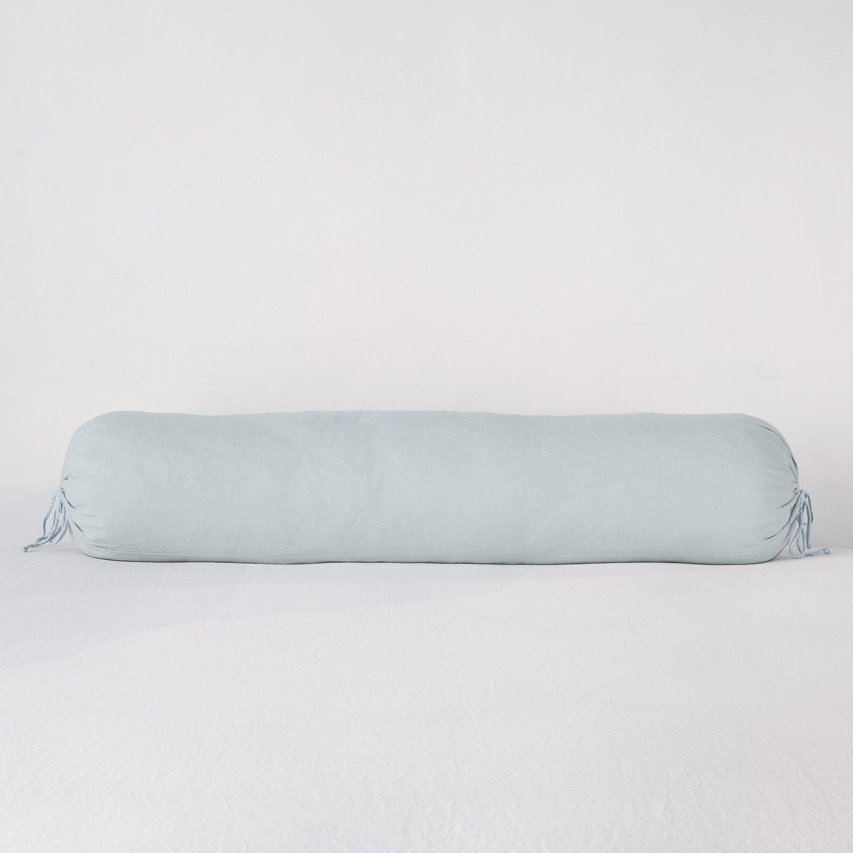 Bella Notte Linen bolster throw pillow in Cloud, gathered tie ends, against white backdrop.