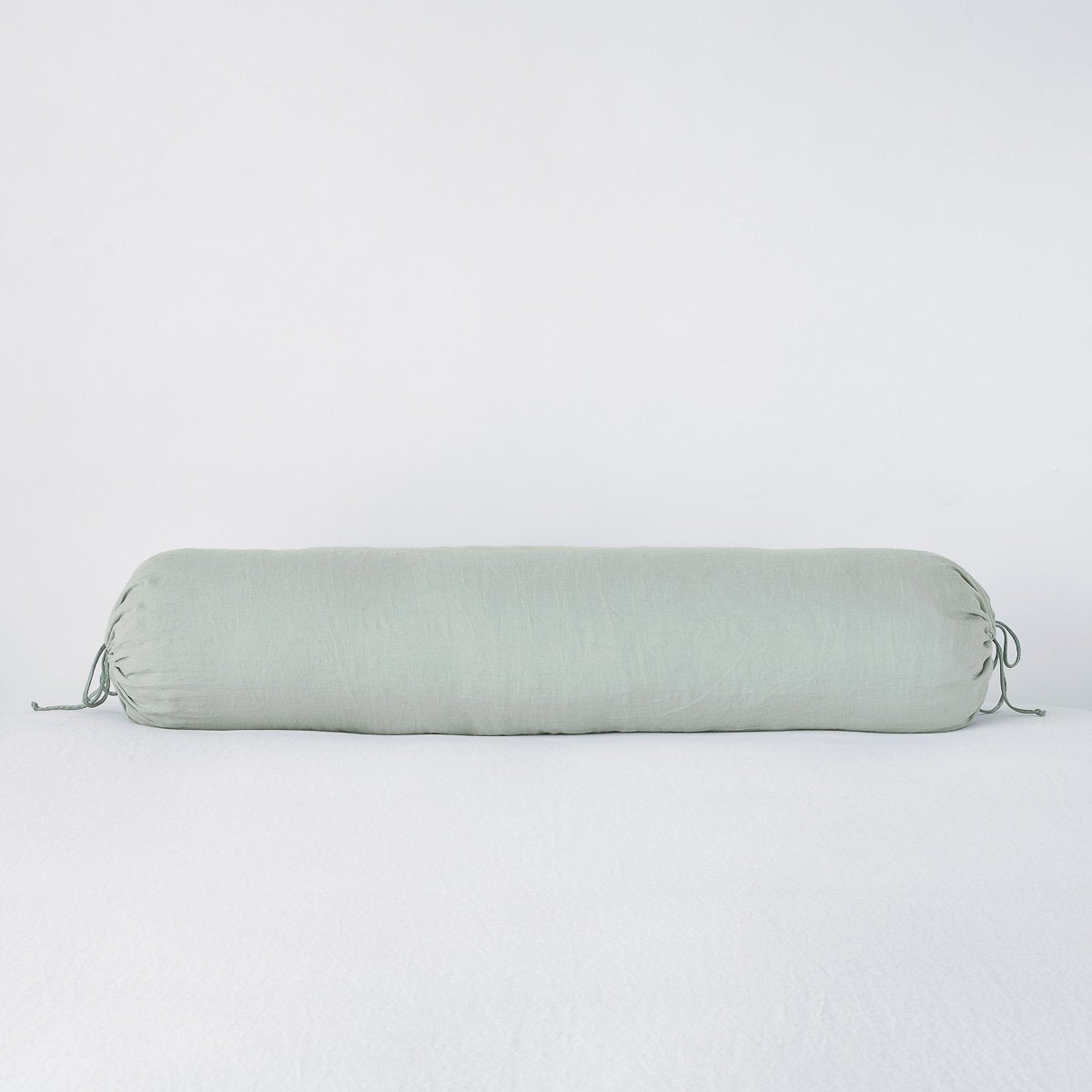 Eucalyptus linen bolster pillow with gathered tie ends, shown against white backdrop.