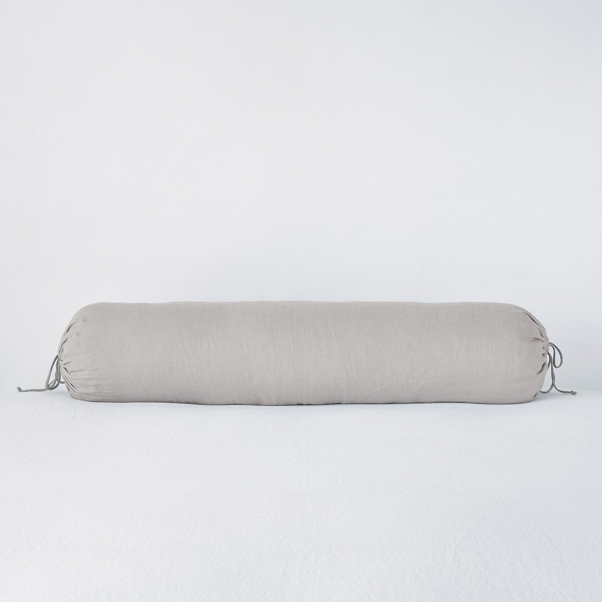 Bella Notte Linen bolster throw pillow in Fog, with tied ends, on white linen.