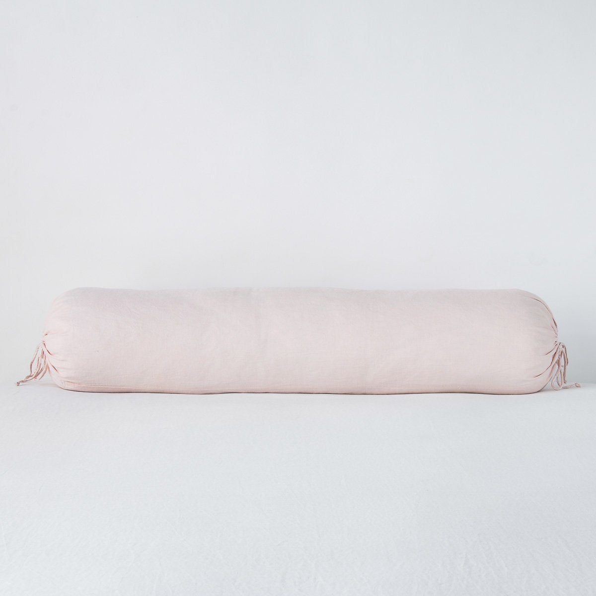 Pearl colorway bolster throw pillow with tied ends, soft linen fabric against white backdrop.