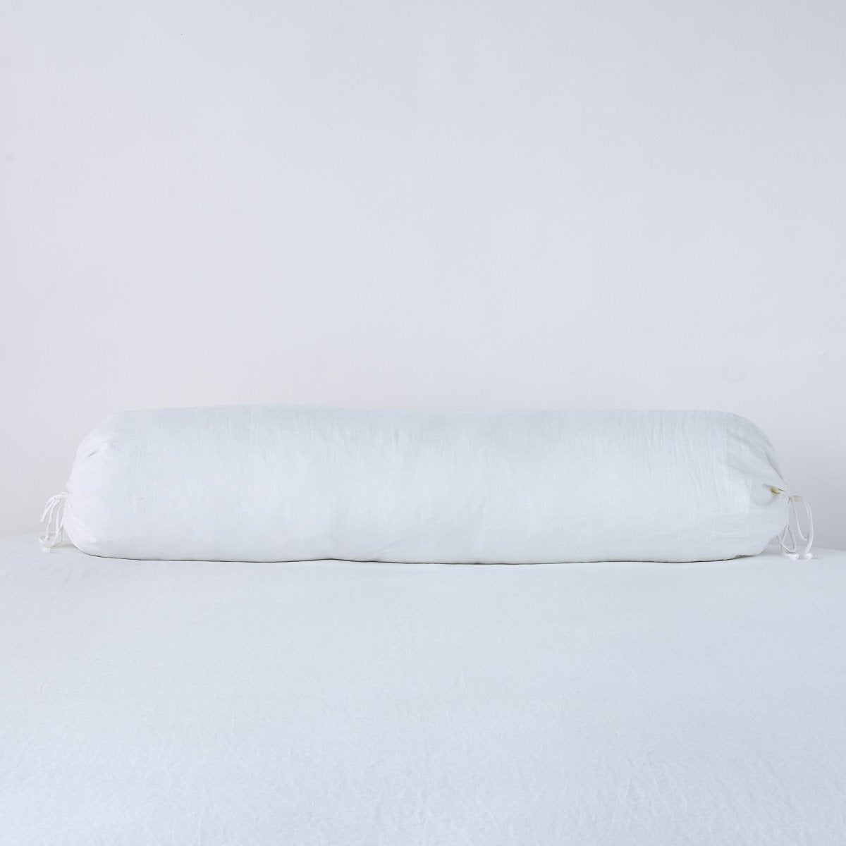 Bella Notte white linen bolster throw pillow, side view on white surface.
