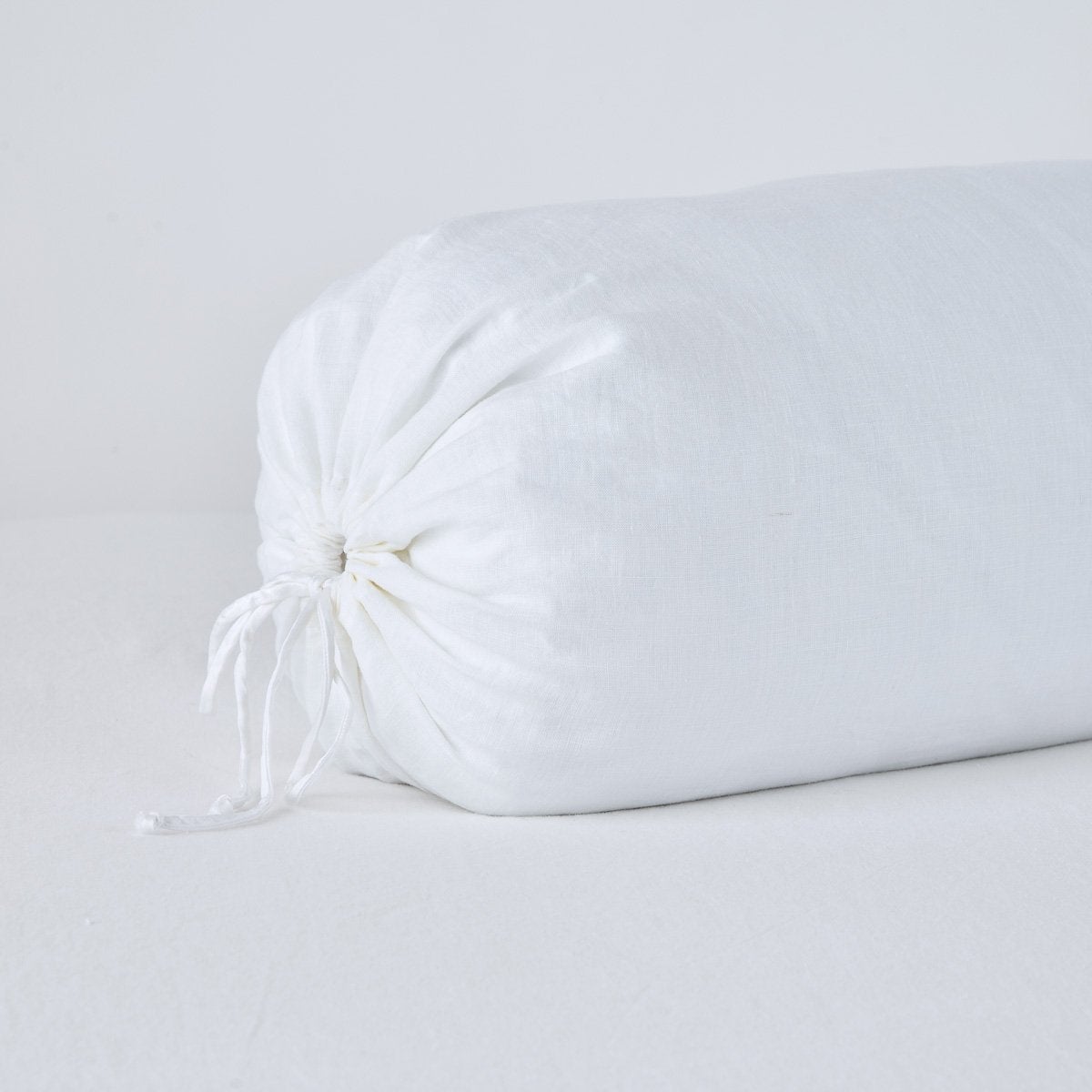 Close-up of White Bella Notte linen bolster pillow with gathered tie closure at end.