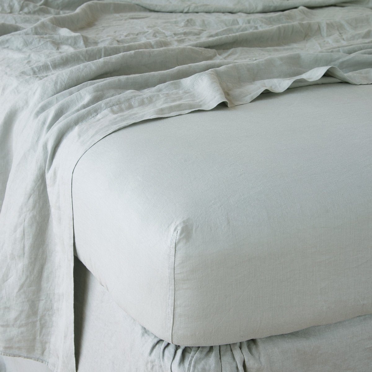 Eucalyptus fitted sheet on bed with matching linen layers, close view of corner and gathered edge.
