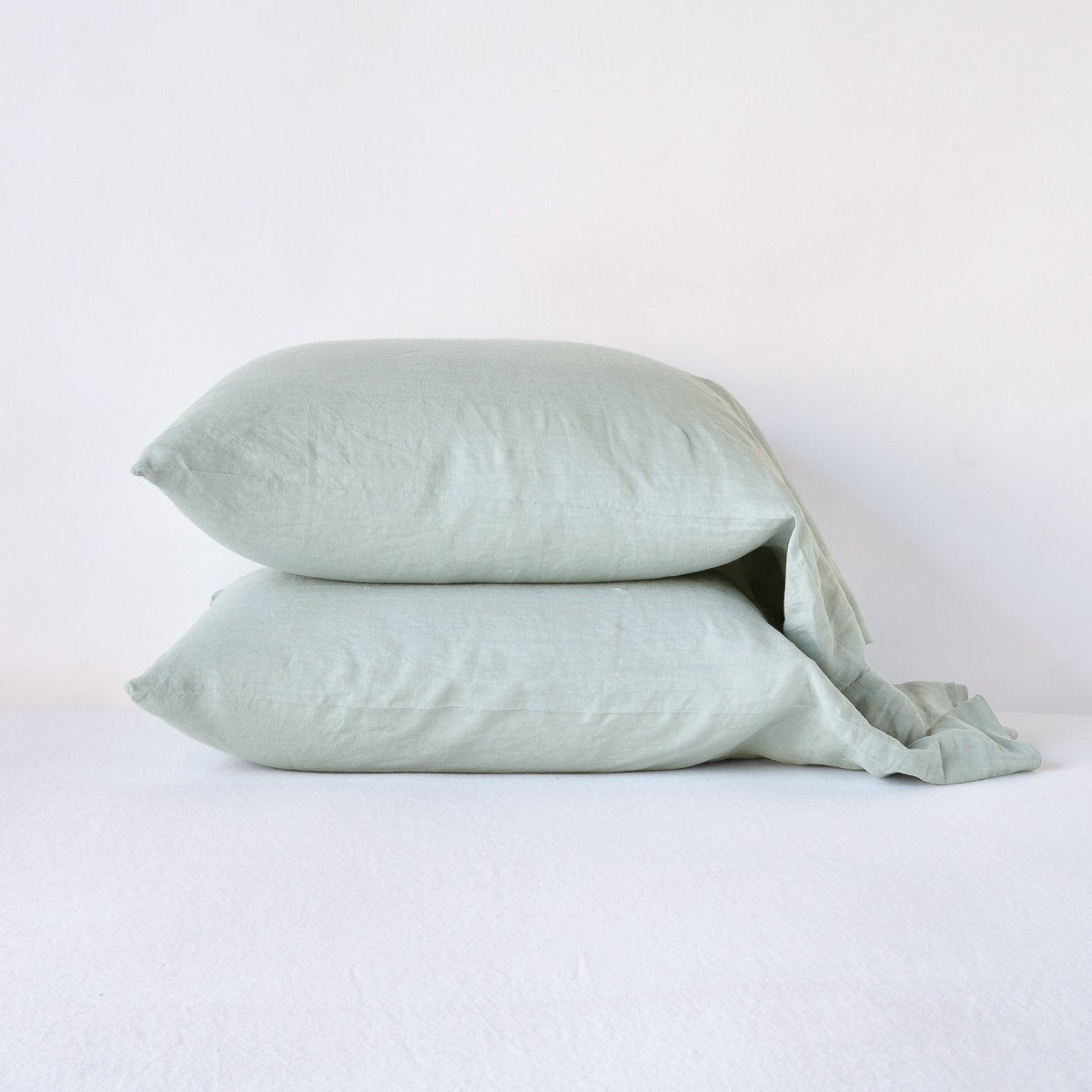 Close-up of two stacked Bella Notte Linen pillowcases in Eucalyptus on a white surface.