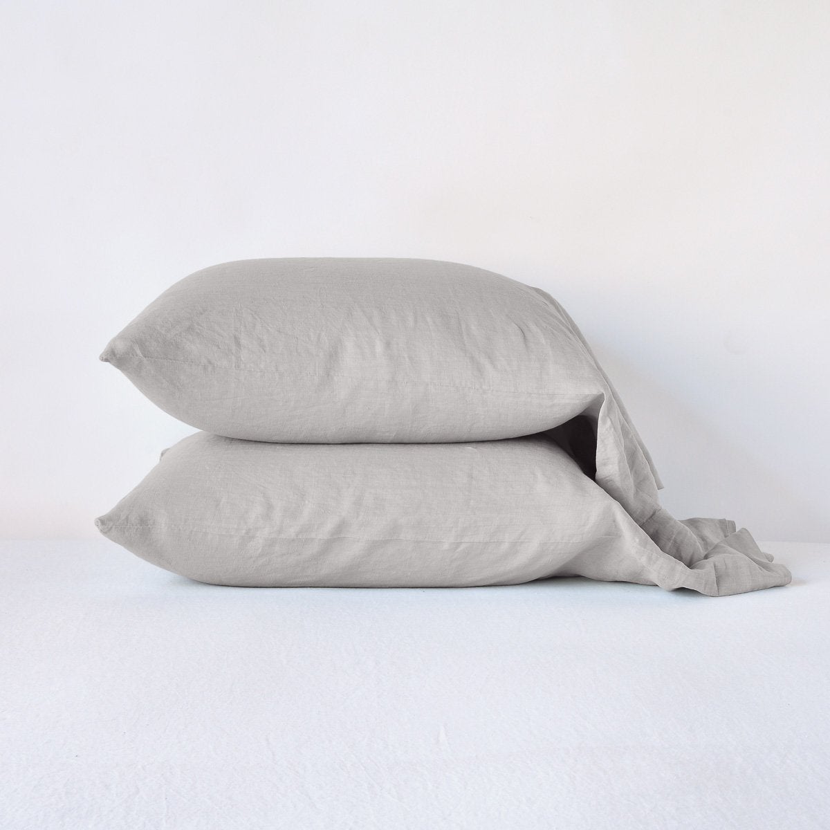 Two Fog linen pillowcases stacked on a bed, showing relaxed drape and texture.