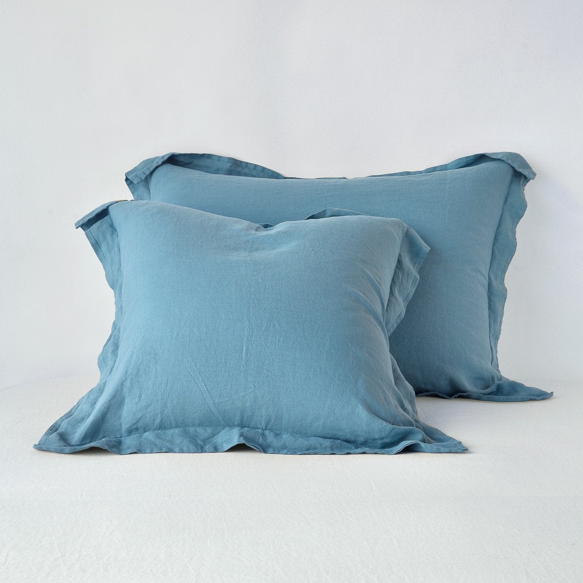 Pair of Bella Notte Linen shams in Cenote, ruffled edges, stacked on white bedding.