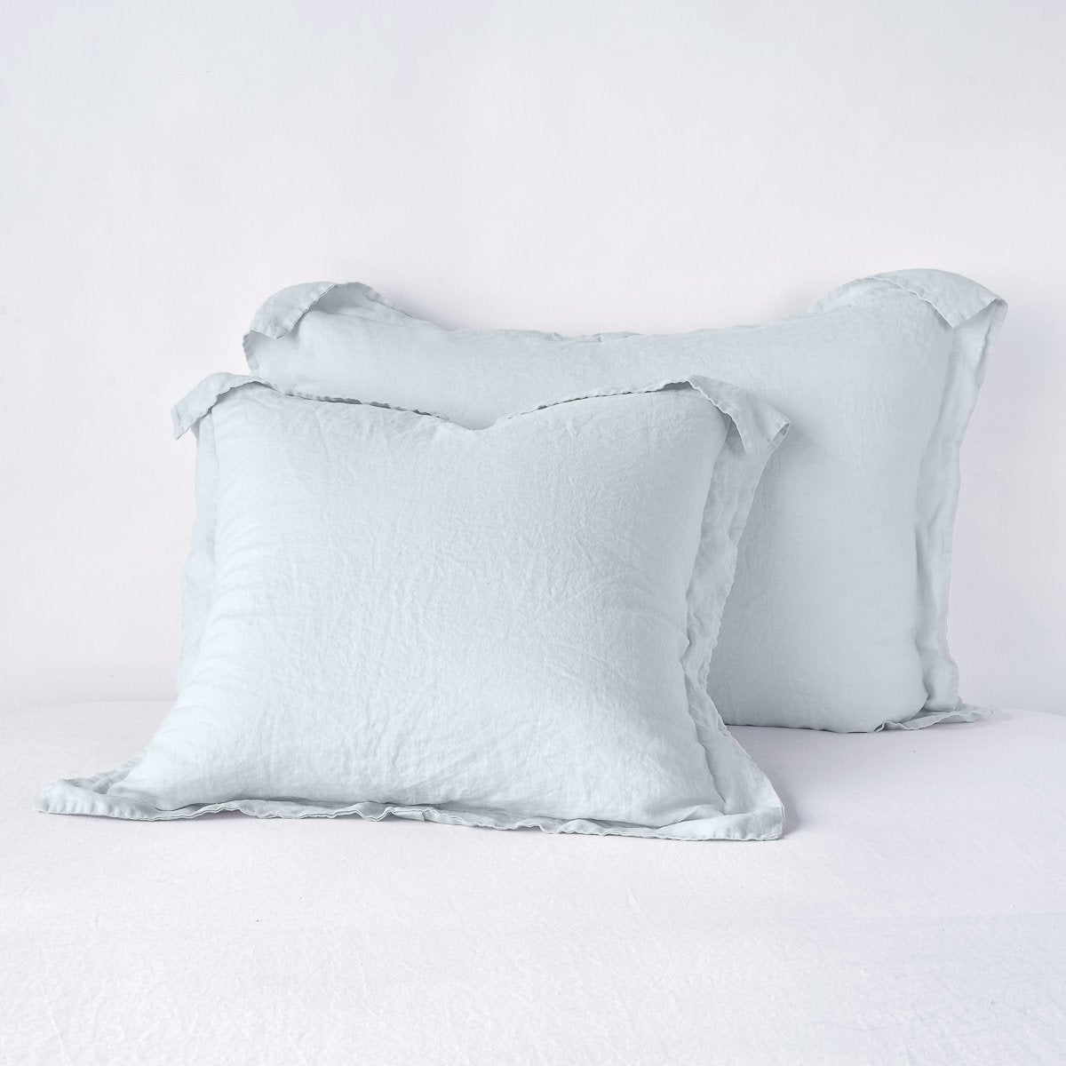 Two Bella Notte Linen shams in Cloud stacked on white bedding, showing relaxed drape and flanged edges.