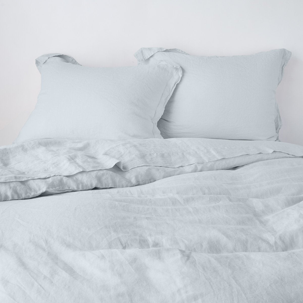 Cloud colourway linen shams with relaxed texture, styled on a made bed with matching duvet.