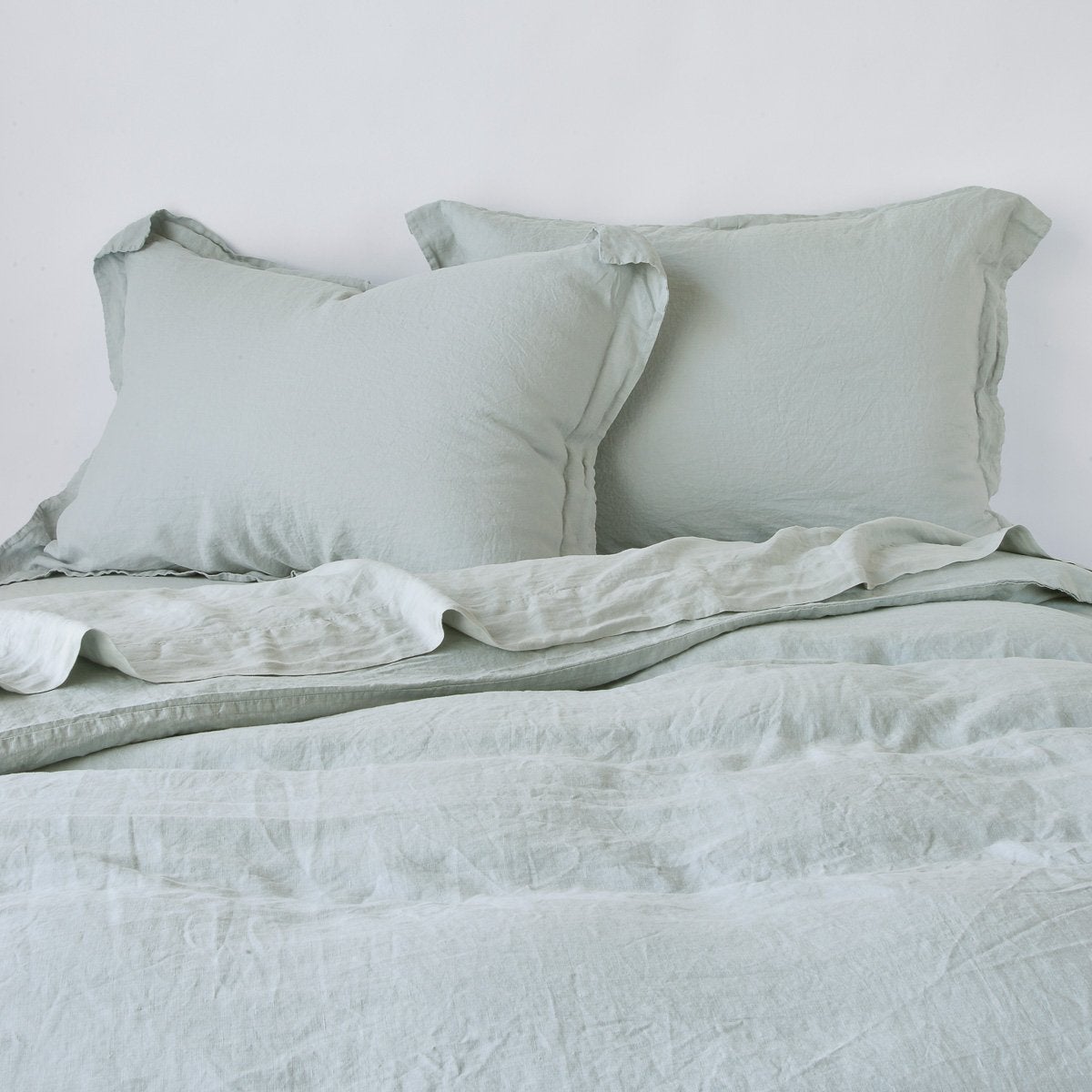 Eucalyptus linen shams styled on a bed with matching duvet, soft relaxed drape.