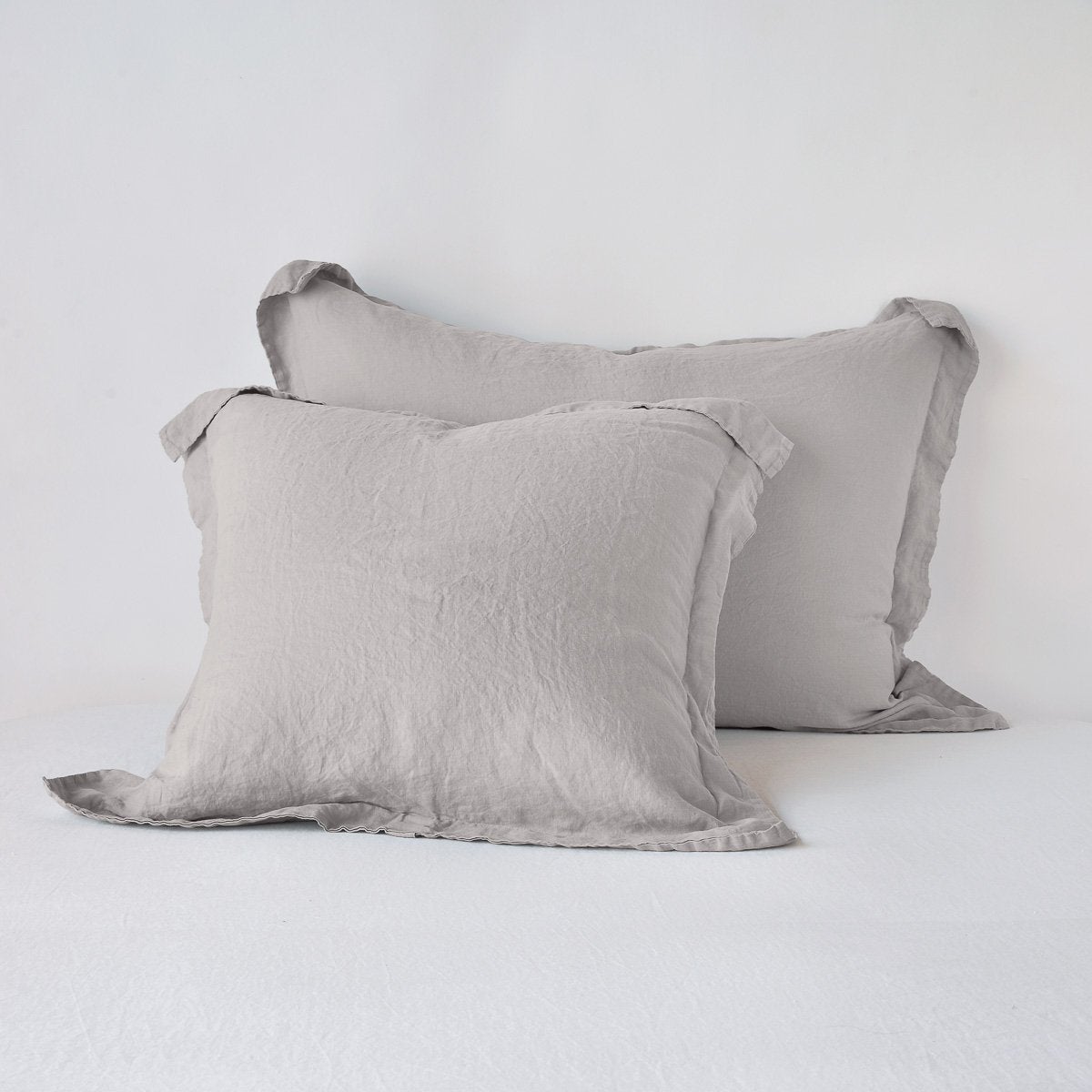 Two Bella Notte Linen shams in Fog, stacked on white bedding, showing relaxed drape and flange trim.