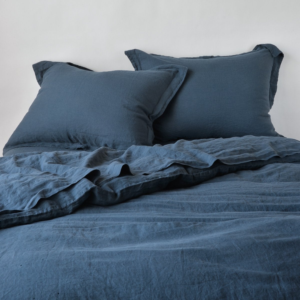 Midnight linen pillow shams styled on a made bed with matching duvet, flanged edges visible.