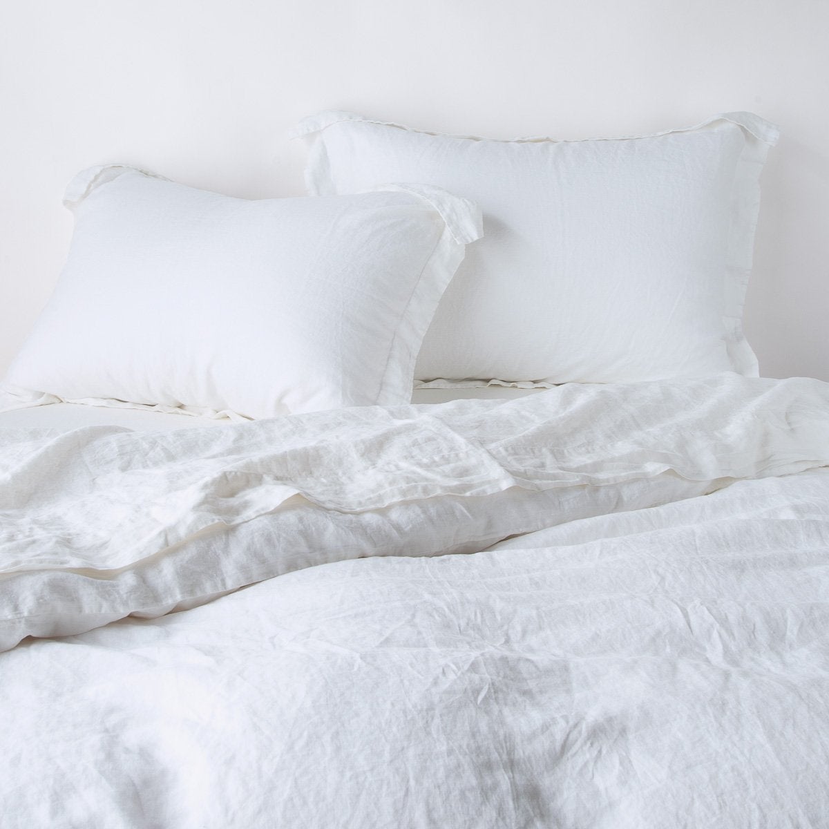 White linen pillow shams with relaxed drape styled on a bed with matching duvet.