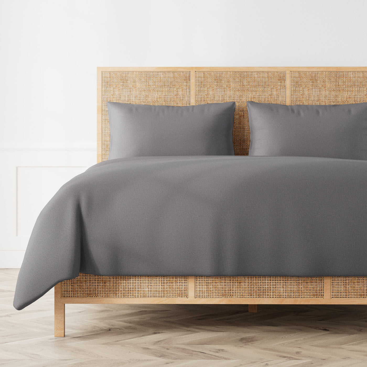 Ann Gish Linen duvet set in slate grey, styled on a rattan bed frame with matching pillowcases.