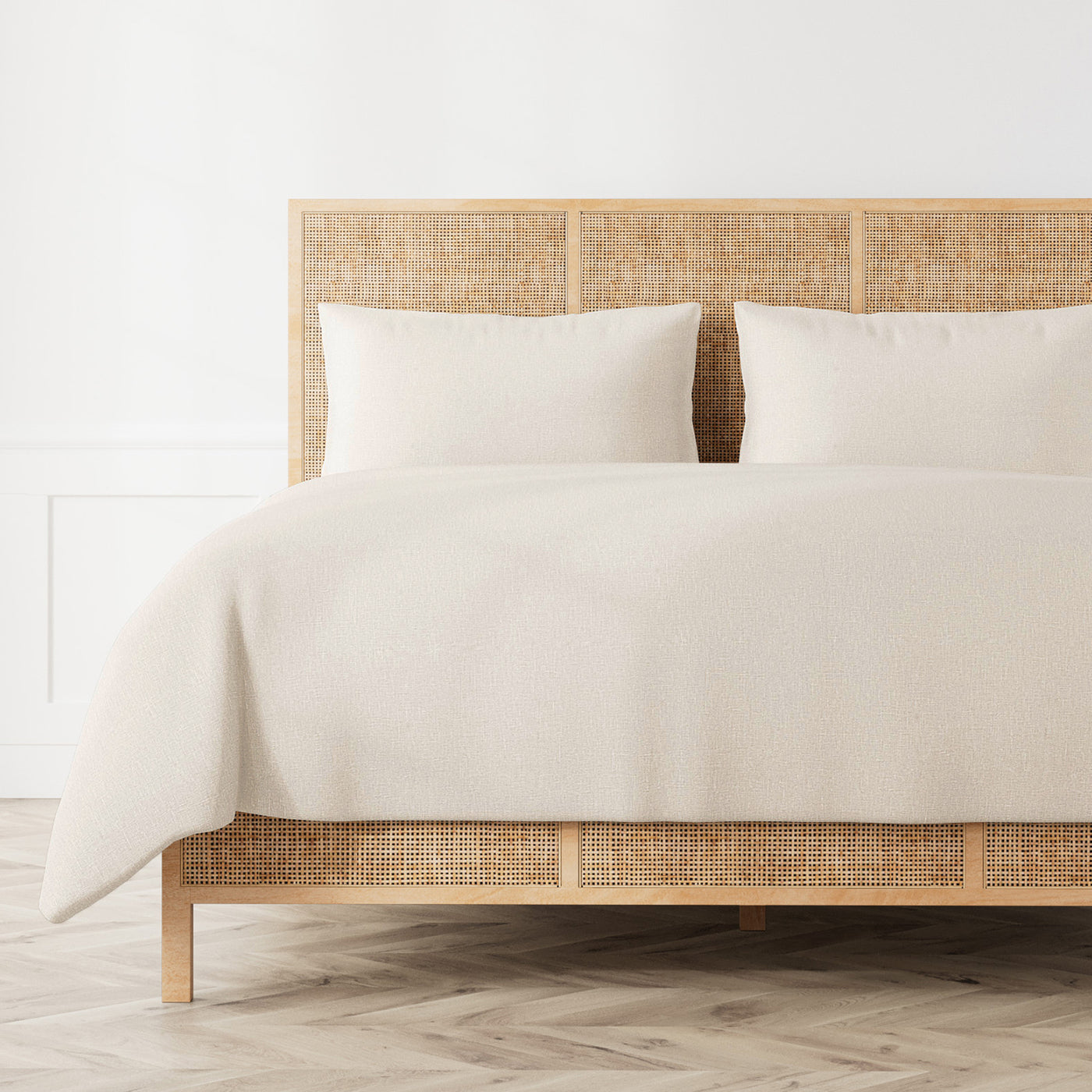 Ann Gish Linen duvet set in ivory styled on a rattan bed, angled three-quarter view.