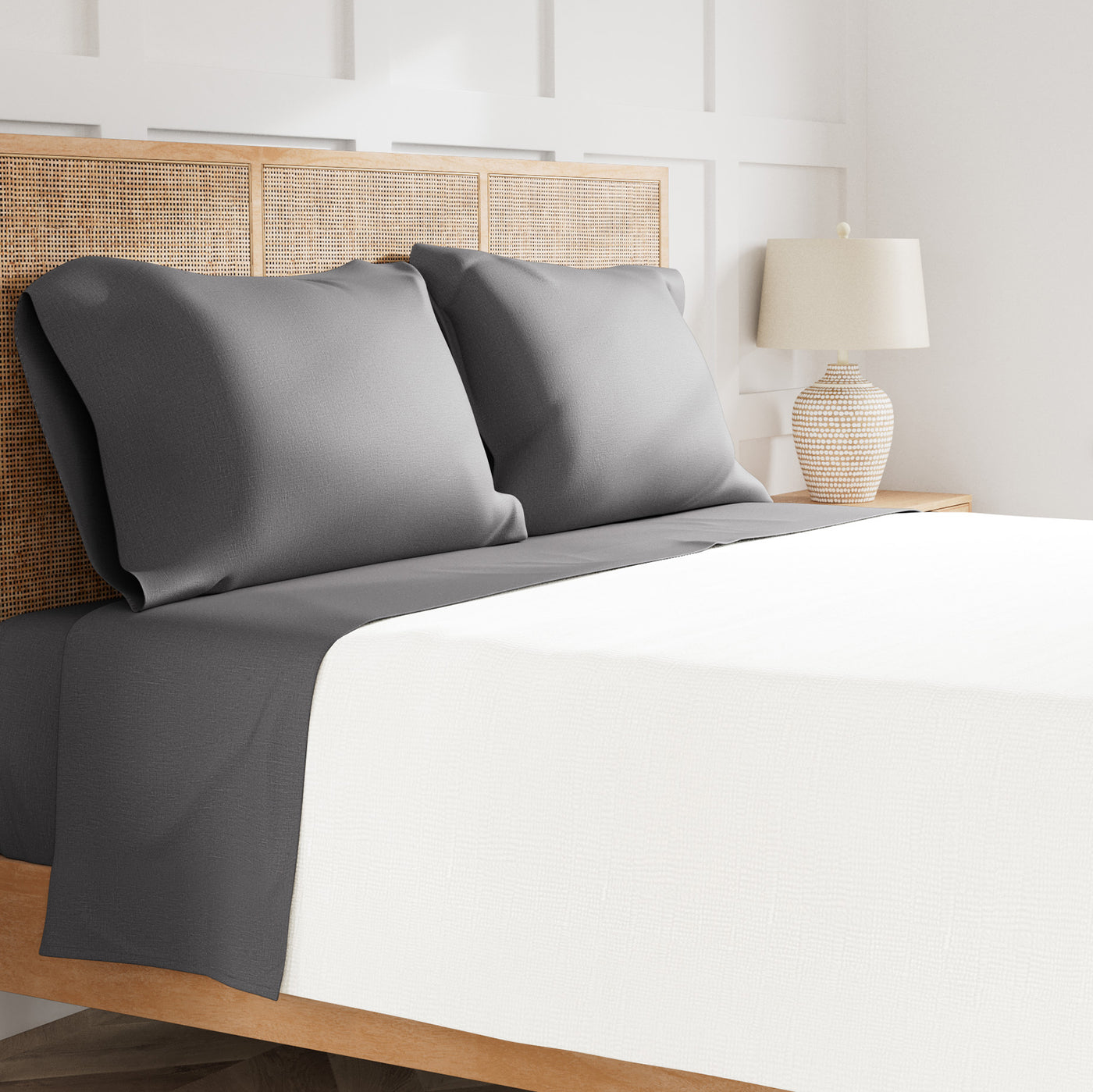 Ann Gish Linen sheet set in charcoal and white, styled on a bed with rattan headboard.
