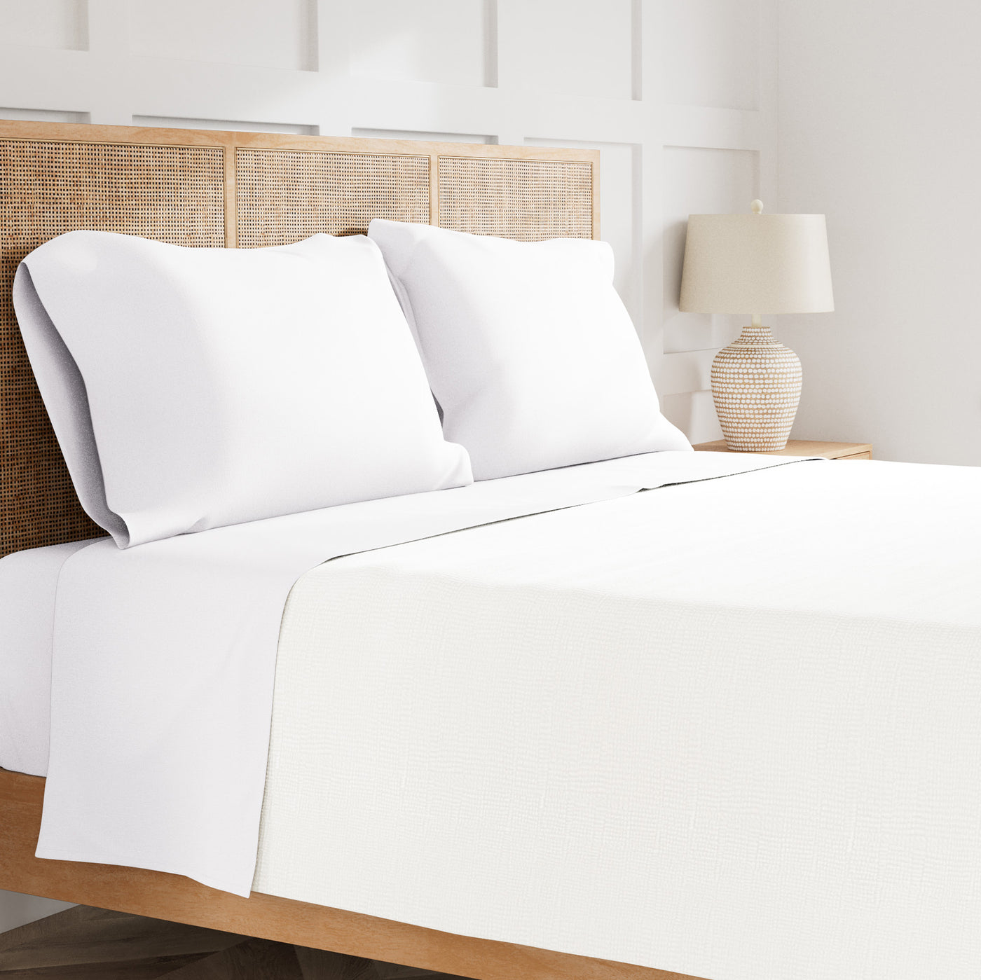 Ann Gish white linen sheet set styled on bed with rattan headboard and two pillows.