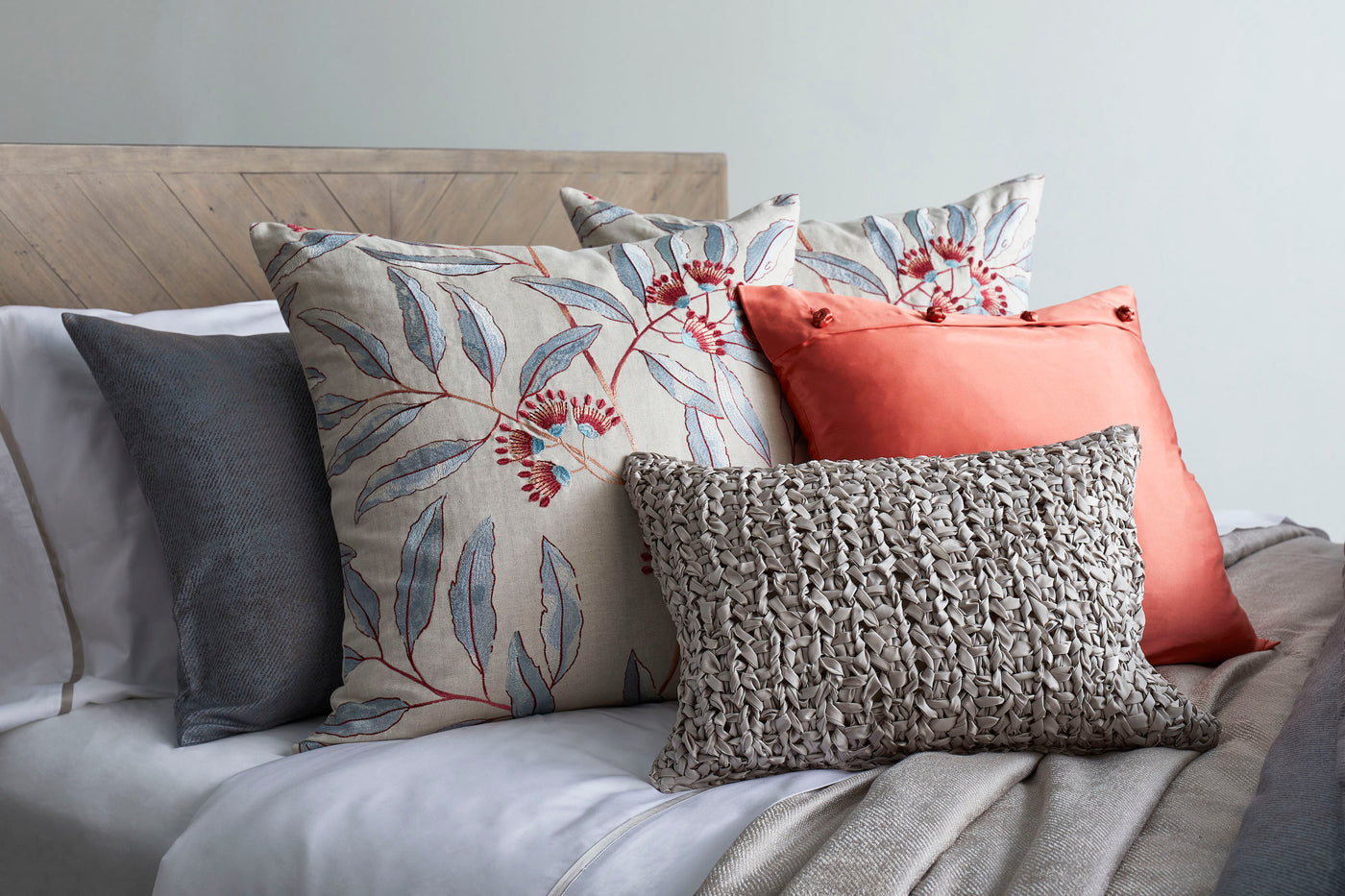 Linenberry pillow styled on bed with coral, grey, and botanical-print cushions.